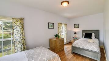 A bedroom with two beds, wooden flooring, a dresser, and a window with floral curtains.
