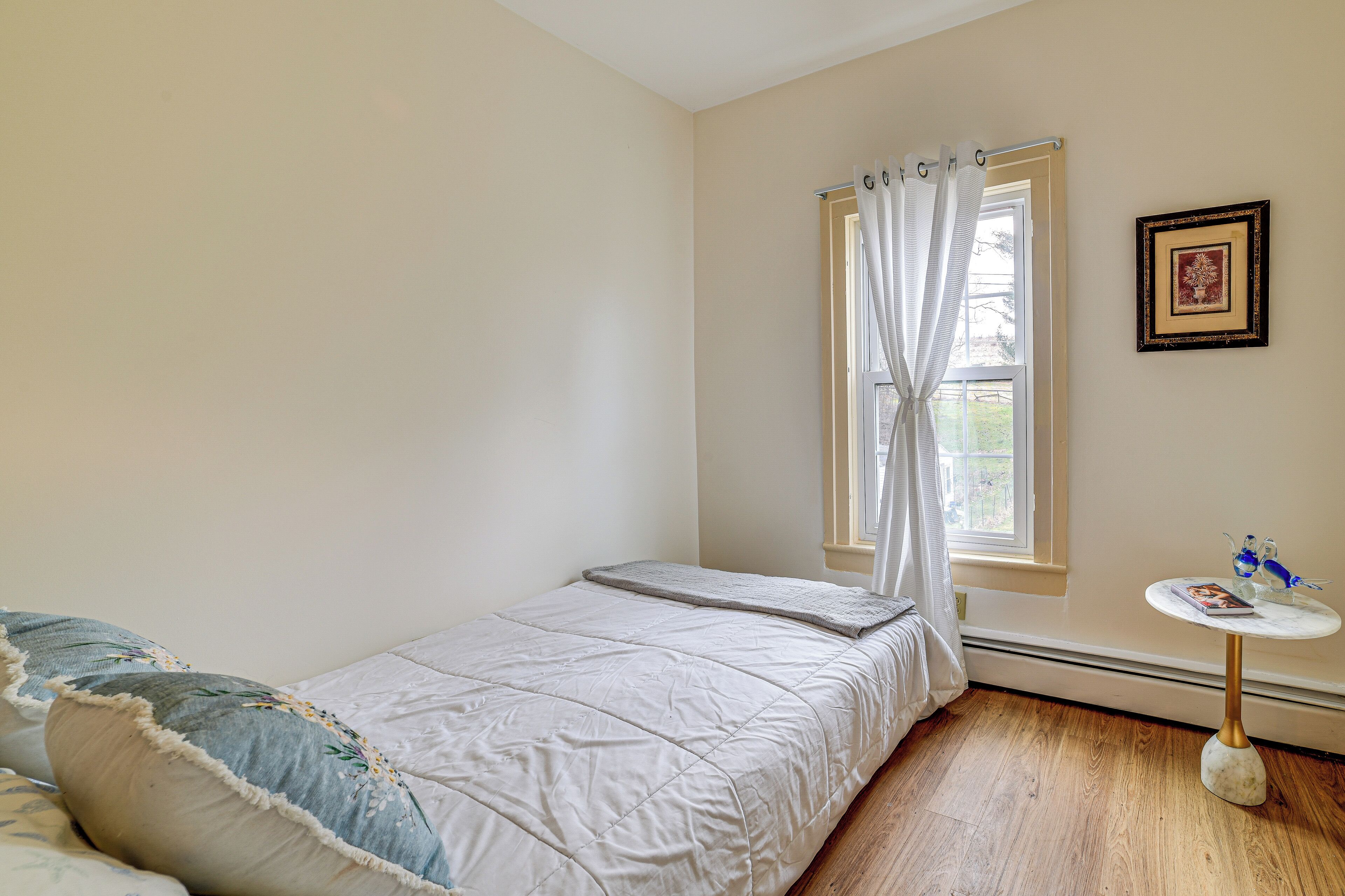Un dormitorio pequeño y ordenado con una cama individual, una mesita y una ventana con cortinas.