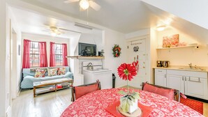 A cozy living room with a sofa, a dining table with a red tablecloth, a ceiling fan, and a kitchen area with white cabinets and a stove. - Cozy Niagara Falls Cottage w/ Gas Grill + Patio! (Niagara Falls)