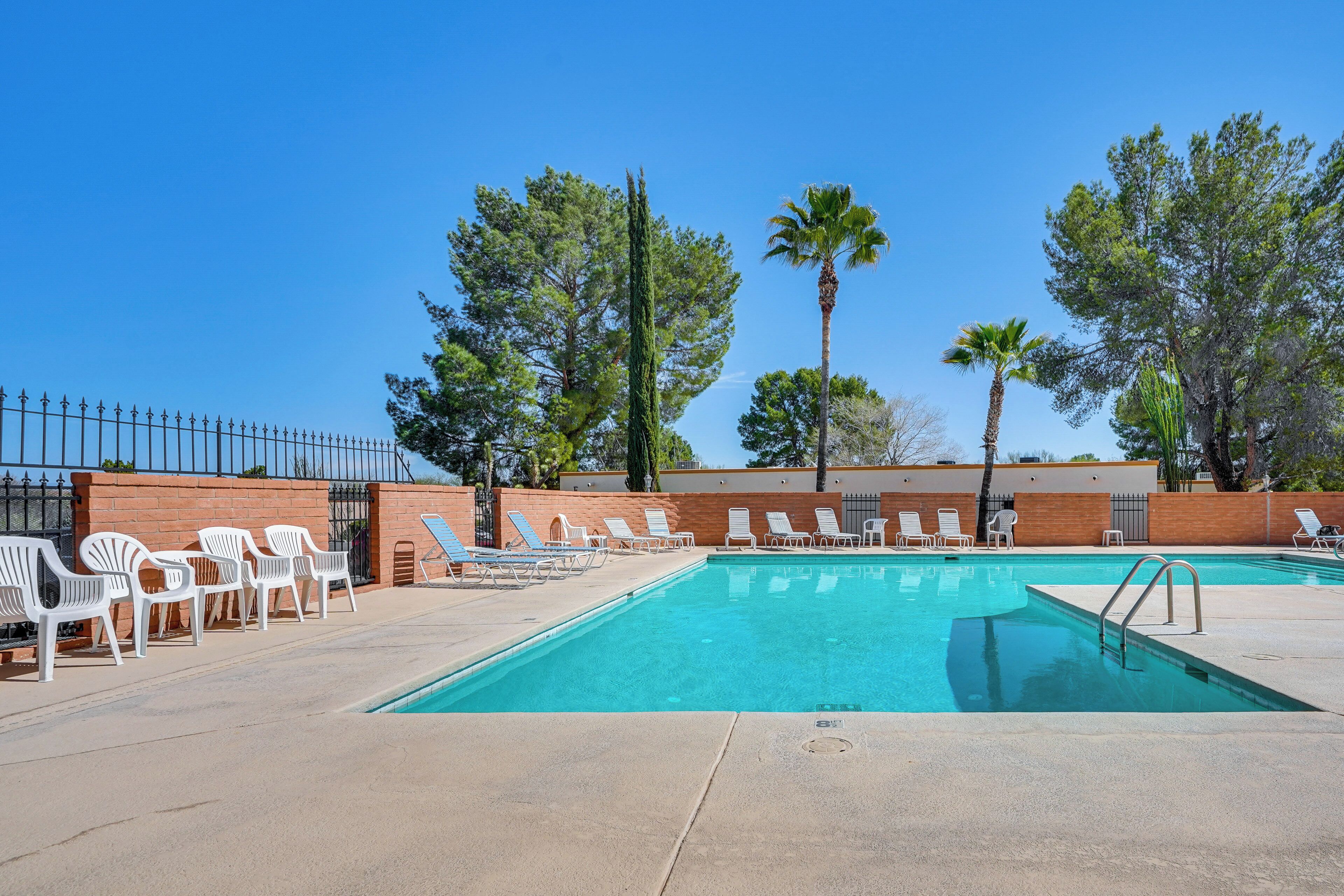 A rectangular pool with clear blue water, surrounded by white lounge chairs and a brick wall.