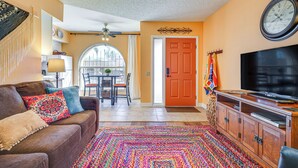 A living room with a brown leather couch, colorful rug, wooden cabinet, and a television. - Charming Green Valley Townhome w/ Community Pool! (Green Valley)