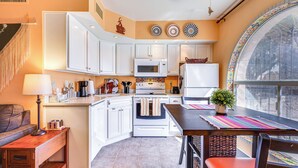 A compact kitchen with white cabinetry, a microwave, a stove, and a refrigerator. There's a dining table with a colorful placemat and a potted plant. - Charming Green Valley Townhome w/ Community Pool! (Green Valley)
