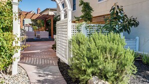 Ein überdachter Patio-Bereich mit einer Pergola, einem weißen Zaun und einem kleinen Garten mit Sträuchern.