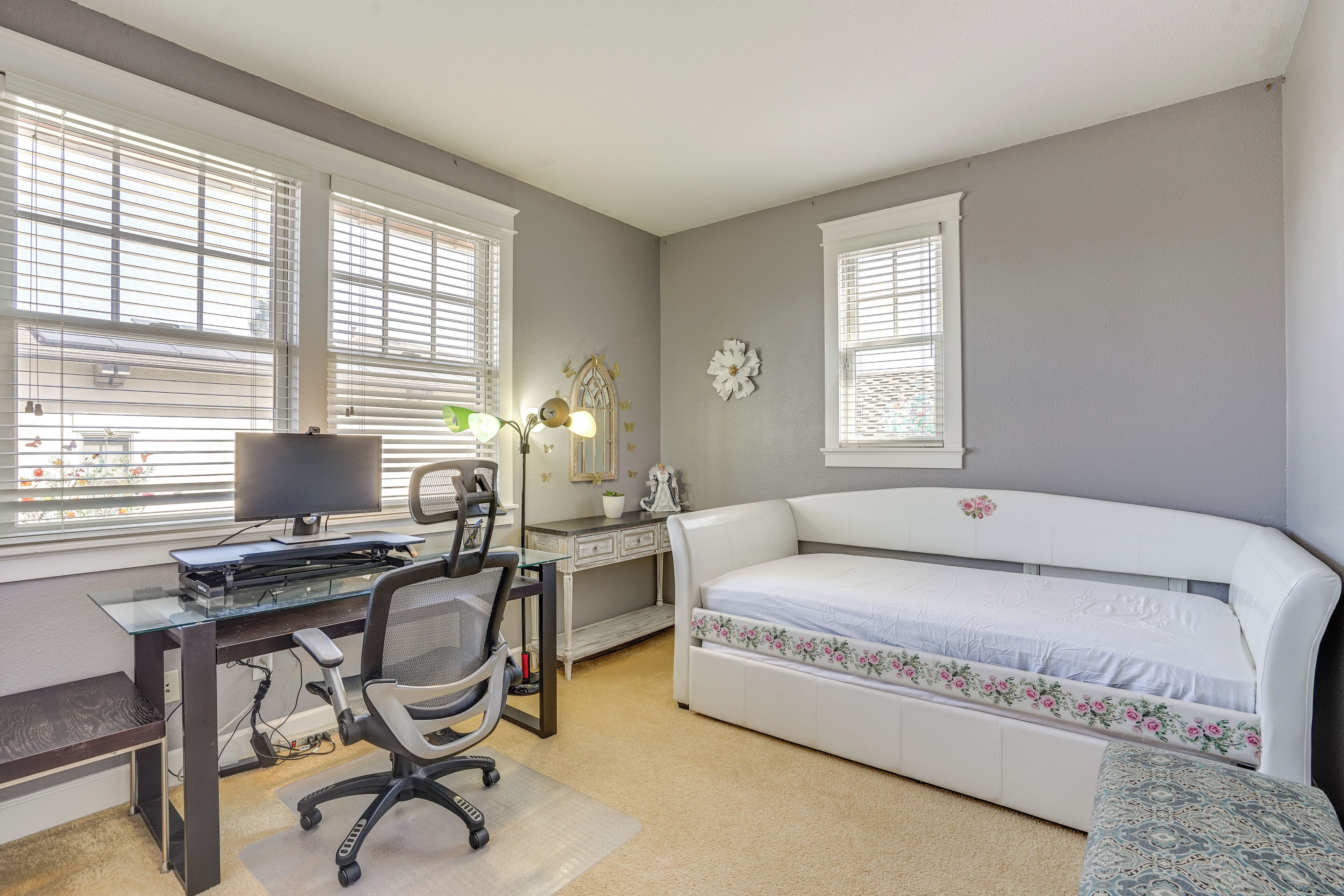 Une chambre avec un bureau, un ordinateur, une chaise et un lit avec une literie à motifs floraux.