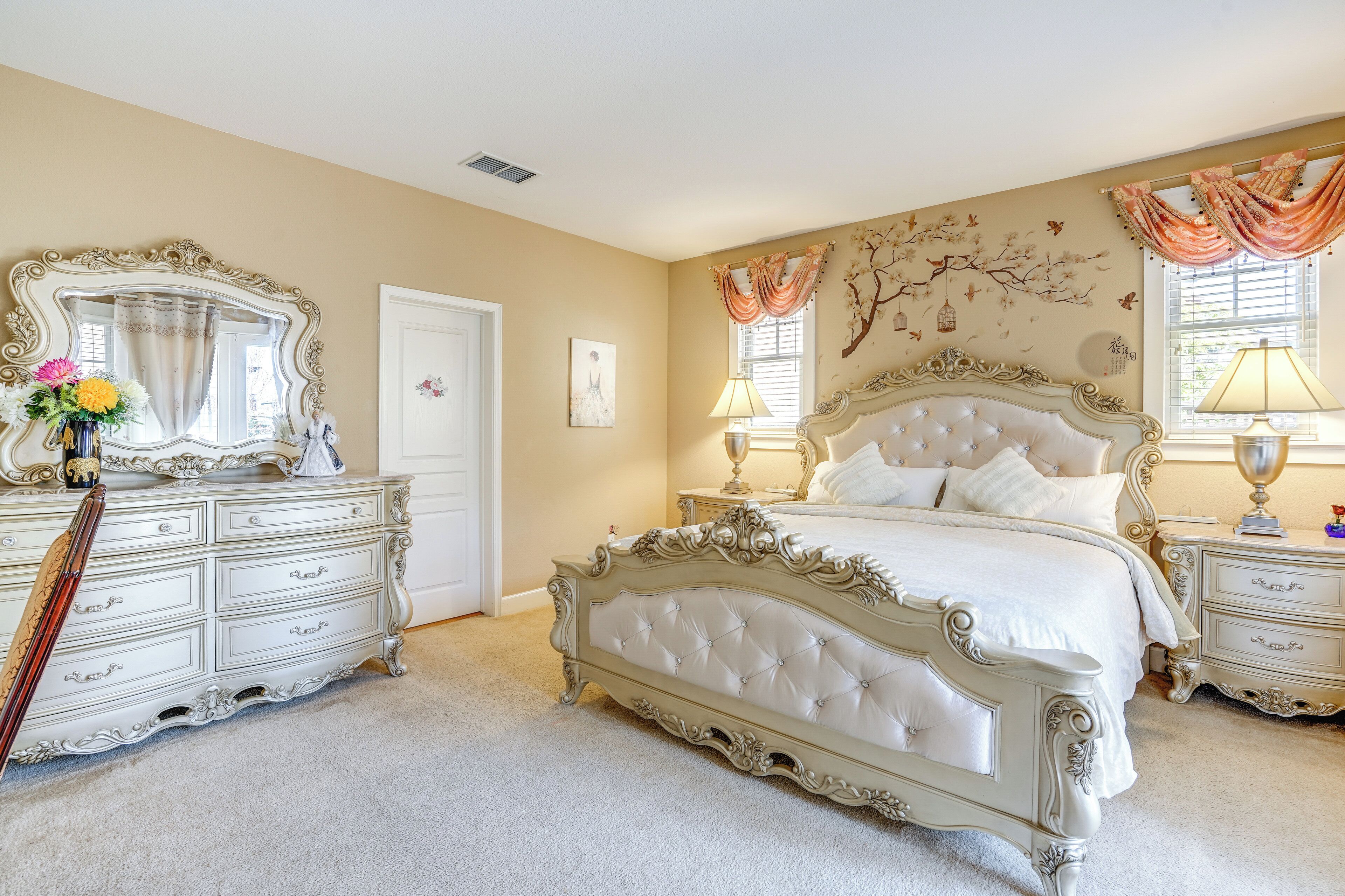 A bedroom with a large ornate bed, a dresser, and a vanity with a mirror.