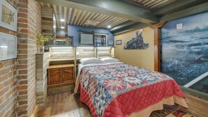 A room with a bed, wooden flooring, a brick wall, and a mural of a boat on water. - Historic Texarkana Studio Rental: Walk to Downtown (Texarkana)