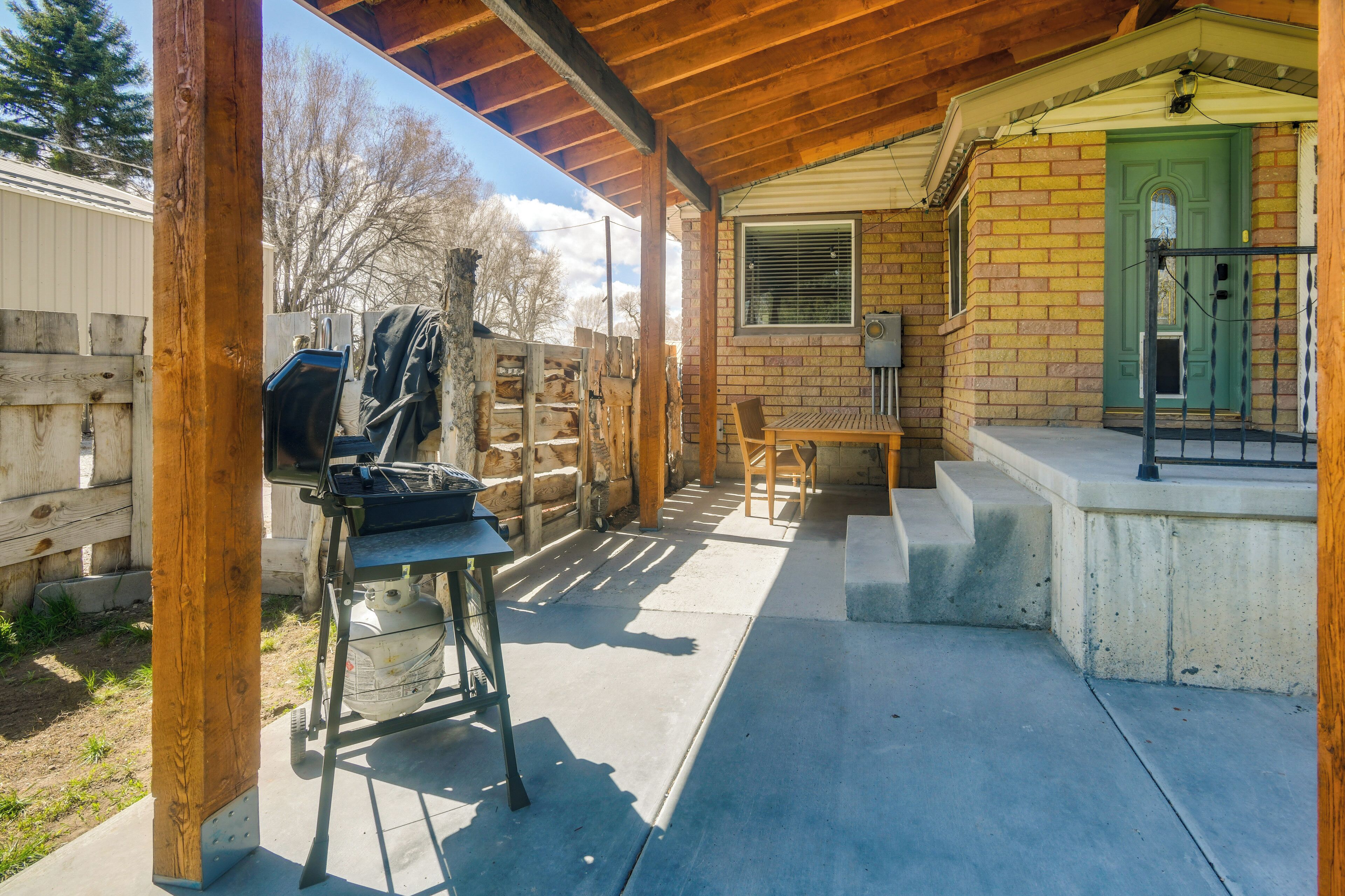 A covered patio with a grill, a table, and a green door.