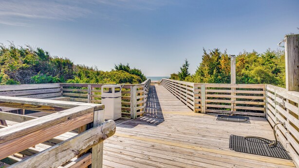 A wooden boardwalk leading to a beach with a railing on one side and dense foliage on the other. - Atlantic Beach Condo w/ Balcony & Beach Access! (Atlantic Beach)