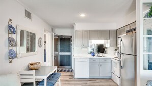 A modern kitchen with white cabinetry, a stainless steel refrigerator, and a dining area with a white table and bench. - Atlantic Beach Condo w/ Balcony & Beach Access! (Atlantic Beach)