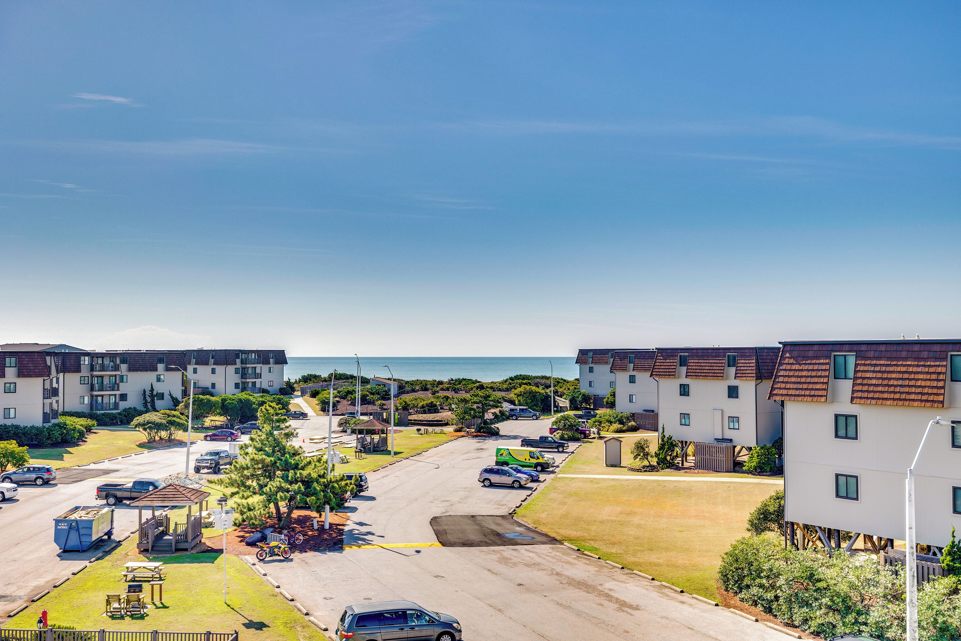 A residential area with apartment buildings, a parking lot, and a beach in the background.
