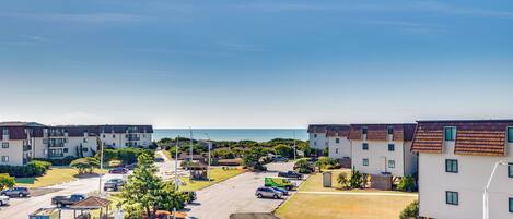 A residential area with apartment buildings, a parking lot, and a beach in the background.