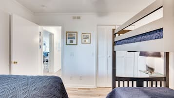 A bedroom with two bunk beds, a door leading to another room, and a small table with a lamp.