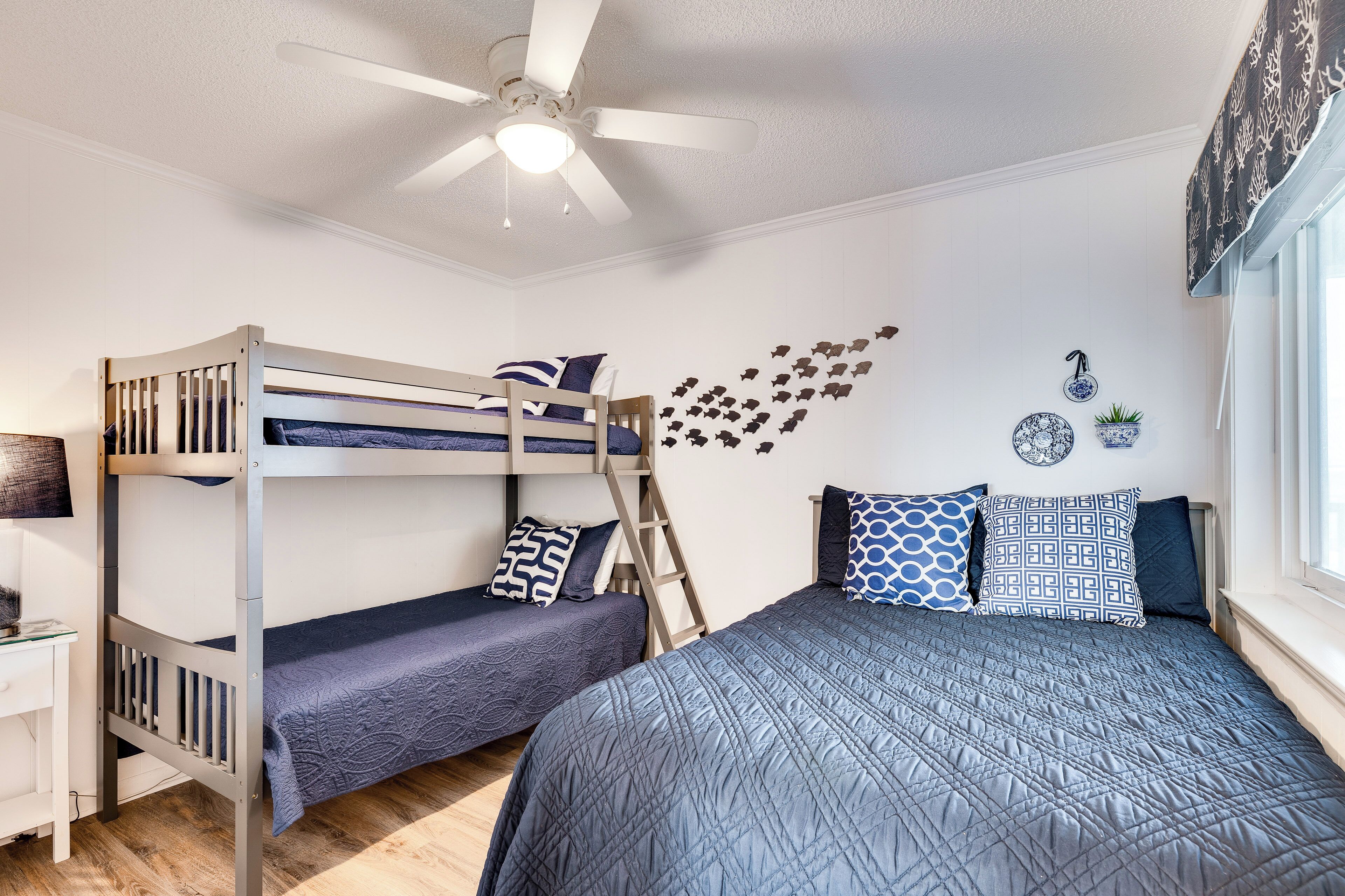 Habitación con literas, un ventilador de techo, escritorio y ventana con cortinas.