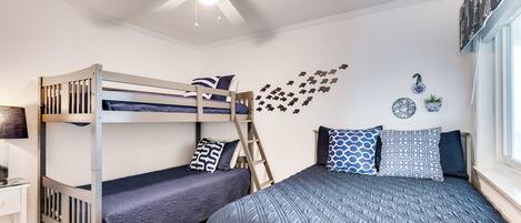 A bunk bed room with a ceiling fan, a desk, and a window with curtains.