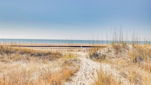 A sandy beach path leading to the ocean with a wooden boardwalk in the distance. - Atlantic Beach Condo w/ Balcony & Beach Access! (Atlantic Beach)
