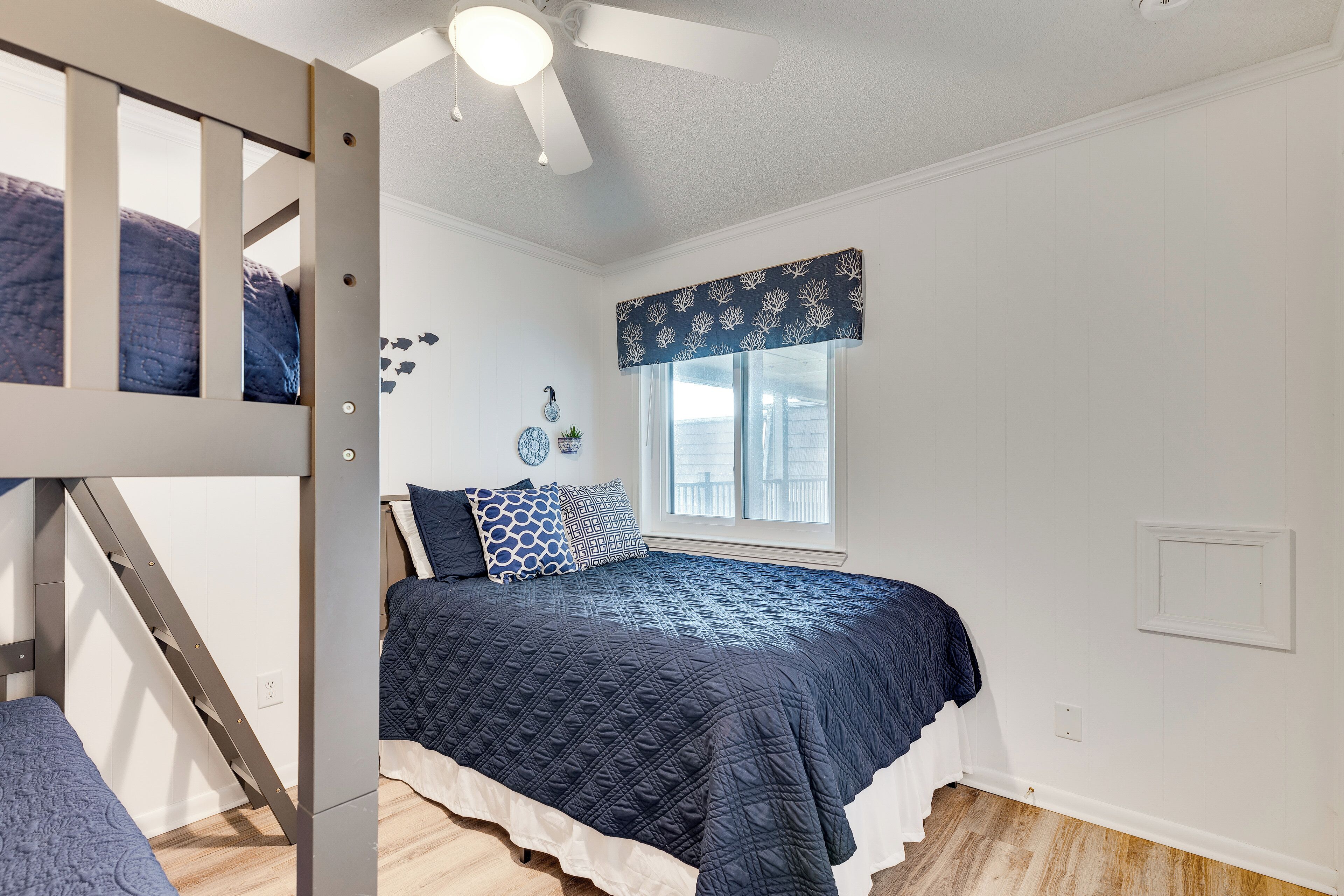 A bedroom with a bunk bed, a large window with a valance, and a ceiling fan.