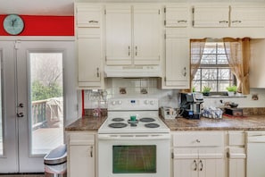 A kitchen with white cabinets, a stove, and a window with curtains. - Furnished Deck & Fire Pit: Greeneville Home! (Mosheim)