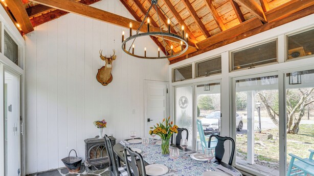 A dining area with a stone floor, wooden ceiling beams, a chandelier, and a deer head mounted on the wall. - Saugerties Farmhouse: Sauna & Countryside Views (Saugerties)