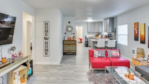 Ein modernes Wohnzimmer mit einem roten Sofa, einem Glastisch und einer Küche im Hintergrund.