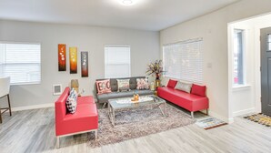 Ein modernes Wohnzimmer mit einem roten Sofa, einem Glastisch und einem grauen Couchen. An den Wänden befinden sich Dekorationen und ein Teppich liegt auf dem Boden.