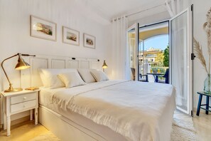 Relax in a spacious bedroom with a large bed, nightstand, and artwork-adorned walls, offering a view of the surrounding greenery.