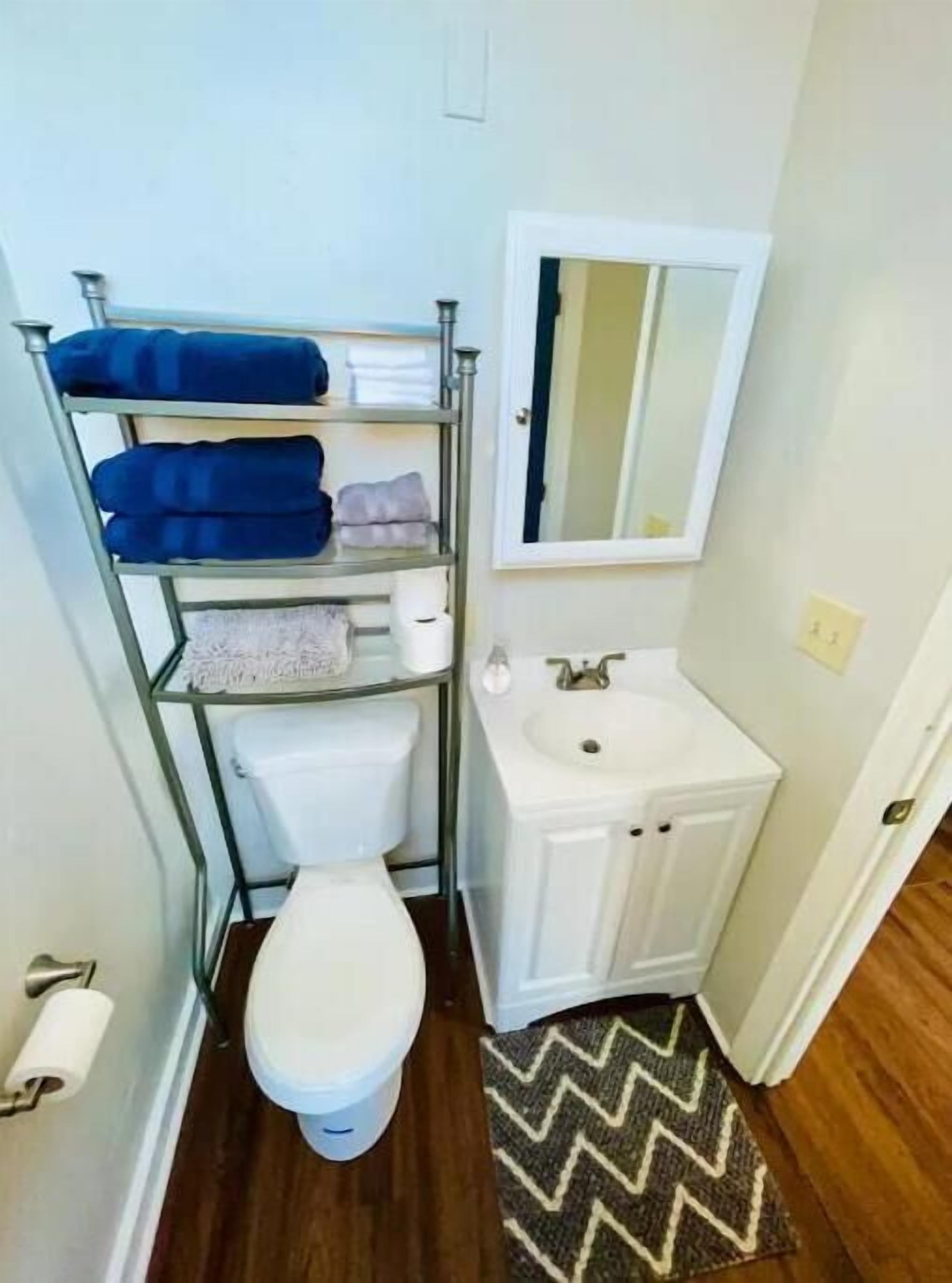 Une salle de bain comprenant des toilettes, un lavabo, un miroir et une étagère avec des serviettes.