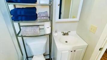 Une salle de bain comprenant des toilettes, un lavabo, un miroir et une étagère avec des serviettes.