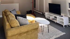 Ett modernt vardagsrum med en soffa, ett soffbord, en tv och en klädhängare.