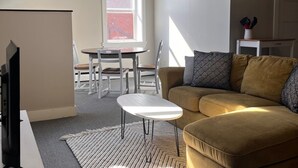 Ett mysigt vardagsrum med en soffa, ett litet bord och en tv. Det finns ett fönster som släpper in naturligt ljus, och en dörr som leder till ett annat rum.