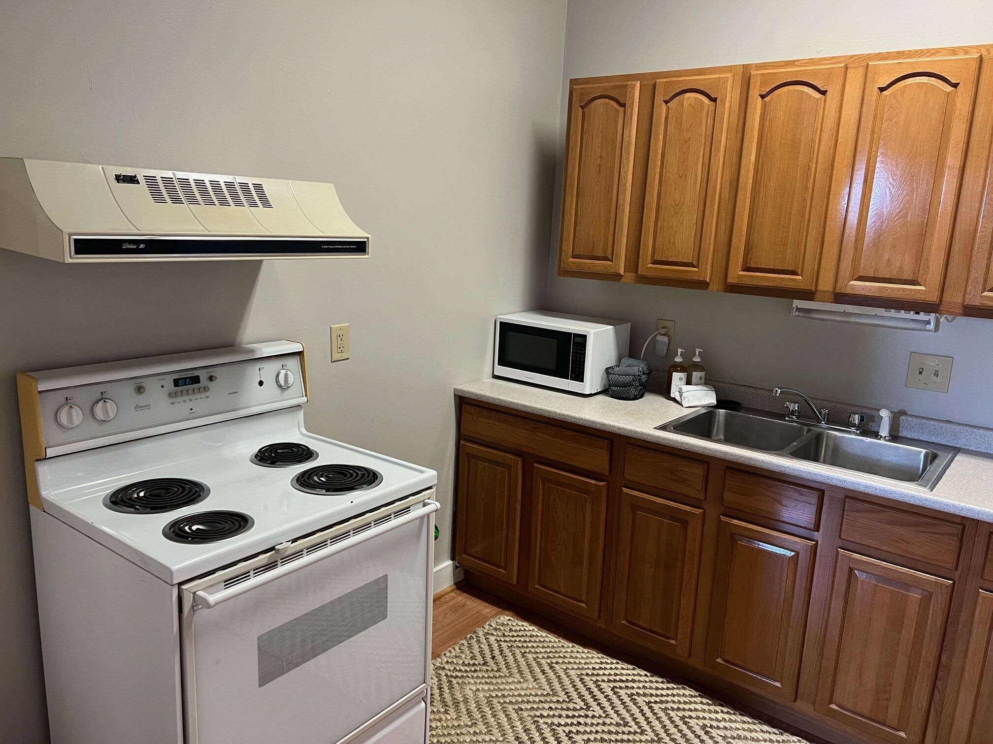 A kitchen with a white stove, a microwave, wooden cabinets, and a stainless steel sink.
