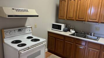 A kitchen with a white stove, a microwave, wooden cabinets, and a stainless steel sink.