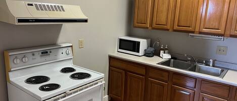 A kitchen with a white stove, a microwave, wooden cabinets, and a stainless steel sink.