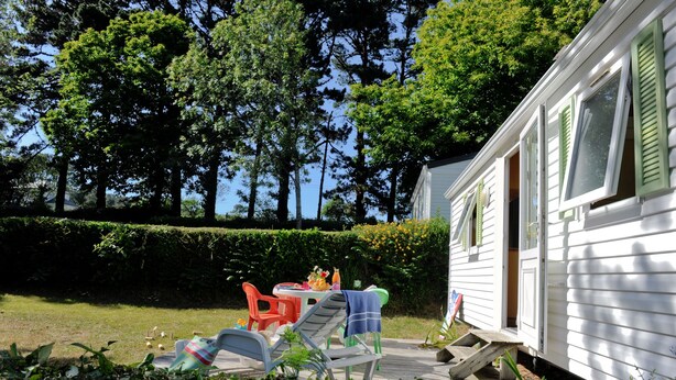 A mobile home with a patio area featuring outdoor furniture, a table with drinks, and a view of a forested area. - Mobil-home Classique 2 Chambres (Telgruc-sur-Mer)