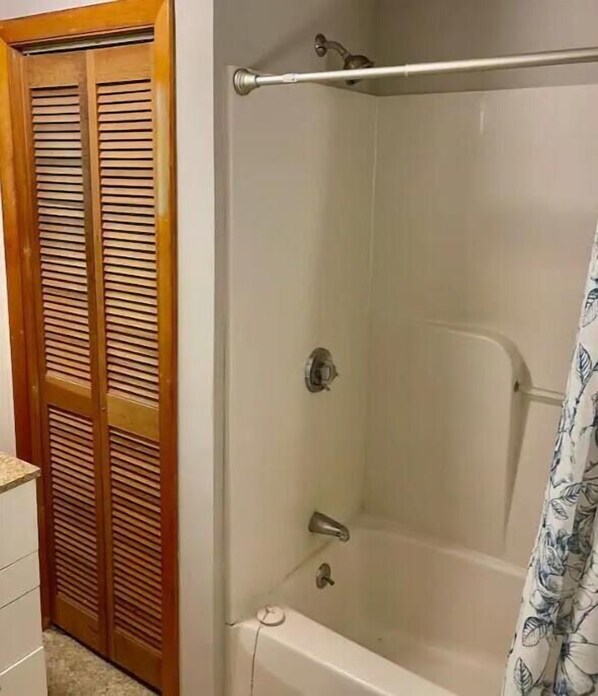 Une salle de bain avec une baignoire, une porte en bois à panneaux ajourés et un rideau de douche à motifs floraux.