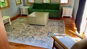 A living room with a green sofa, a white coffee table, a patterned rug, and wooden flooring. - Sweet comfy cottage on Small Point Road (Phippsburg)