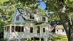 A two-story house with a porch, surrounded by trees and a grassy yard. - Sweet comfy cottage on Small Point Road (Phippsburg)