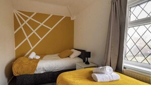 A hotel room with two beds, a headboard with a geometric pattern, a window with curtains, and a nightstand with a lamp. - Immaculate 2-bed Duplex Apartment in Leeds (Leeds)