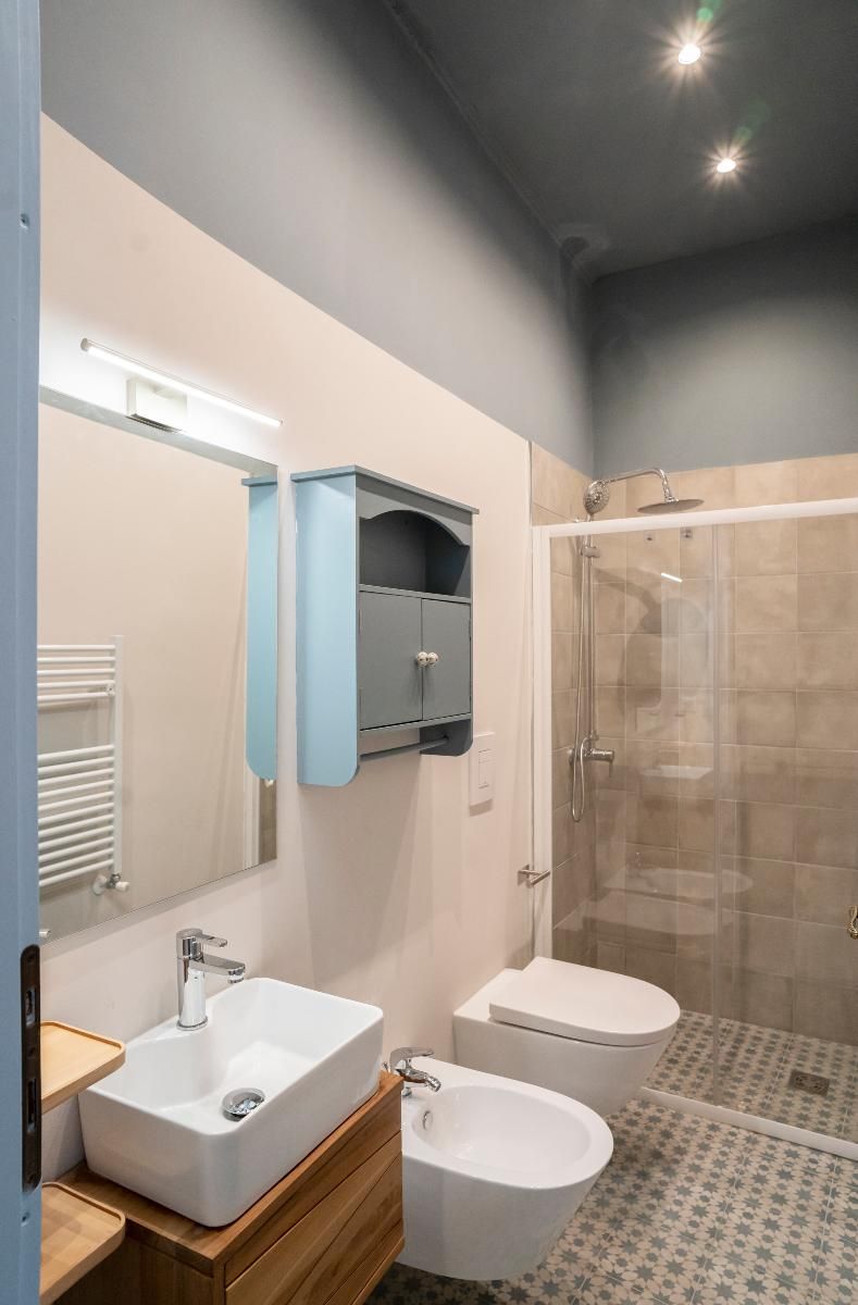 A modern bathroom with a large mirror, a sink, a toilet, and a shower enclosure.
