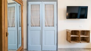 Une pièce dotée d’une porte à deux battants, d’un téléviseur fixé au mur et d’une étagère en bois.