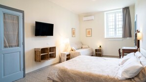 Une chambre à coucher avec un grand lit, deux tables de chevet avec des lampes, un téléviseur fixé au mur et une fenêtre avec des rideaux.