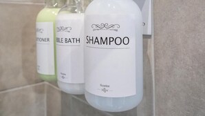 Tres botellas de champú, acondicionador y gel de baño sobre una pared de azulejos.