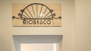 Un pasillo con baldosas de diseño, una puerta con marco azul claro y un cartel que dice “RIO BASCO”.