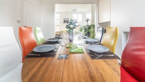 Uma área de refeições com mesa de madeira posta para quatro pessoas, rodeada por cadeiras coloridas.