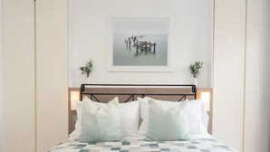 Uma cama bem arrumada com colcha xadrez, cabeceira de metal e duas luminárias de cabeceira.