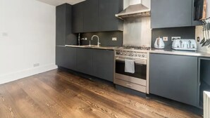 Uma cozinha moderna com armários escuros, fogão de aço inoxidável e piso de madeira.