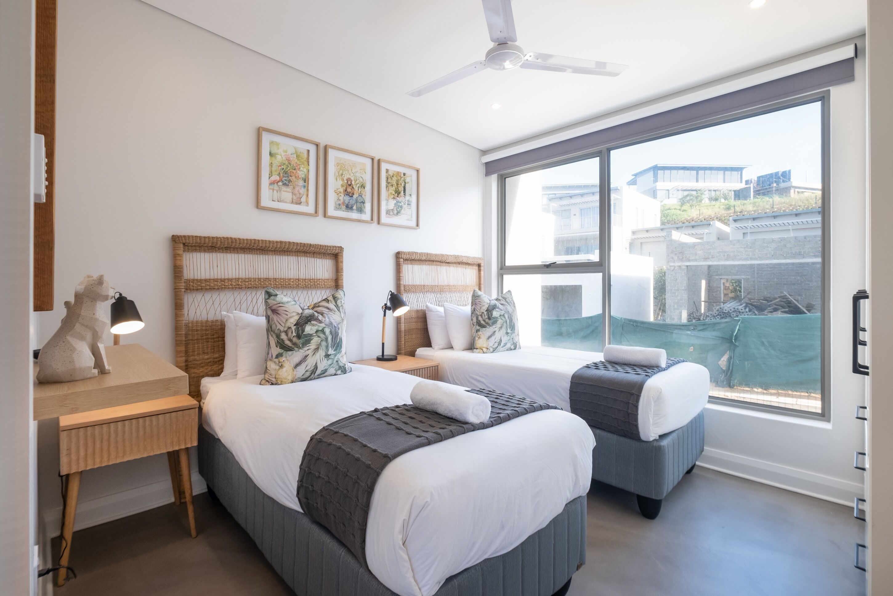 Ein modernes Hotelzimmer mit zwei Betten, einem Schreibtisch und einem großen Fenster mit Blick auf die Stadt.