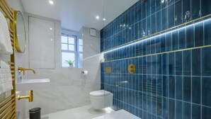 Ein modernes Badezimmer mit einem weißen Waschtisch, einem goldenen Wasserhahn, einer blauen Fliesenwand und einer weißen Toilette.