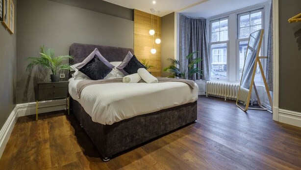 Ein modernes Schlafzimmer mit einem großen Bett, einem Nachttisch, einem Heizkörper und einem Fenster mit Vorhängen.