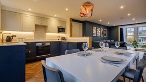 A modern kitchen with white cabinets, a central island, and a dining area with a white table set for four. - Modern 6BR/4Bath in the heart of #LakeDistrict (Cumbria)