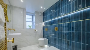 A modern bathroom with a white vanity, a gold faucet, a blue-tiled wall, and a white toilet. - Modern 6BR/4Bath in the heart of #LakeDistrict (Cumbria)